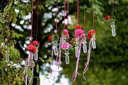 Photo for A bouquet of pink flowers in small glass vases hanging in a row on a lamppost in a park. Decorative adornment. - Royalty Free Image