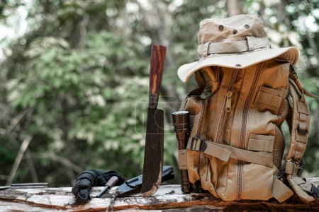 Foto de Equipo para supervivencia sombrero mochila cuchillo de senderismo camping linterna descansando sobre madera de madera en el fondo es un bosque - Imagen libre de derechos