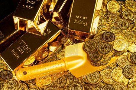 Foto de Pala de oro recogiendo pilas de monedas de oro y pilas de barras de oro - Imagen libre de derechos