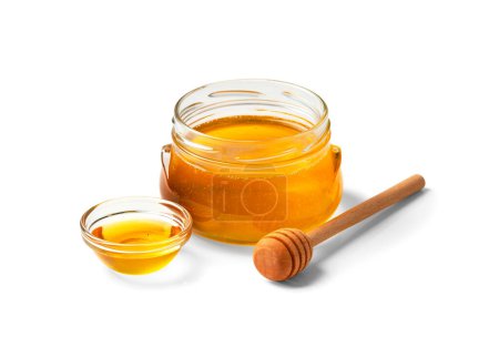 Téléchargez les photos : Miel biologique dans un bocal en verre et un bol transparent, trempette en bois sur fond blanc. Cuillère pour le miel et le miel frais dans des pots ouverts sur l'isolement close-up. Produits sains. - en image libre de droit