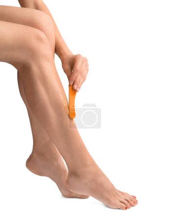 Téléchargez les photos : The girl does depilation of the legs in isolation. The girl's hand applies wax for depilation on the leg on a white background. Skin shugaring. Body care. Cosmetic procedures for the care of the skin of the feet. Smooth legs. - en image libre de droit