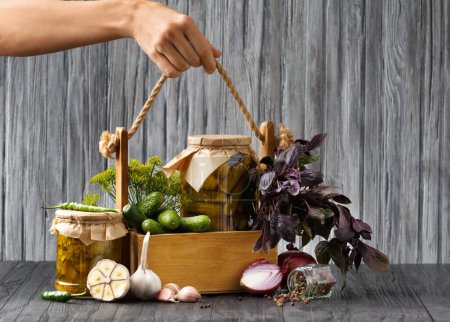 Téléchargez les photos : Fresh cucumbers, basil, pickled cucumbers in a jar in a wooden box on a gray background. Box with vegetables in hands on a wooden background. Fresh gherkins, garlic, onion, basil and sliced cucumber appetizer. - en image libre de droit
