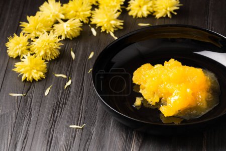 Téléchargez les photos : Crystallized honey in a black plate on a dark wooden background. Composition of honey, yellow flowers and petals on a black background. Useful natural products. Healthy food. - en image libre de droit