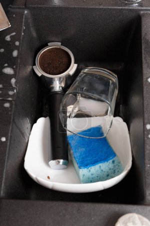 Photo for Washing dishes concept. Dirty dishes with foam from detergent in a black stone sink in the kitchen top view. Dirty glasses, cups, plates, cutlery in the kitchen sink. - Royalty Free Image
