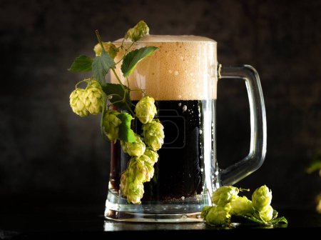 Téléchargez les photos : Dark beer in a mug and green hop on wooden table on brown background. Oktoberfest. Beer Festival. - en image libre de droit