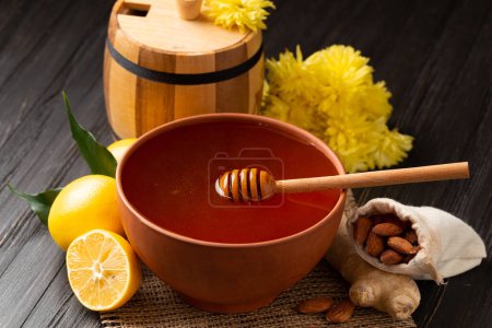 Foto de Wooden barrel for honey, clay bowl with honey, dipper, lemon, yellow flowers on a wooden background. Still life of useful products. Composition of honey in different dishes, lemon, flowers close-up. - Imagen libre de derechos