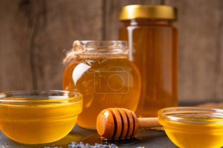 Photo for Honey in glass jars and bowls of different sizes and a wooden dipper lies in a drop of honey on a wooden background. The concept of natural organic honey. - Royalty Free Image