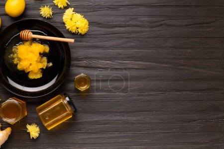 Téléchargez les photos : Conceptual composition of crystallized honey in a black plate, liquid flower honey in jars, lemon, lime, ginger on a dark background top view with space for text. Different honey on a black background. - en image libre de droit