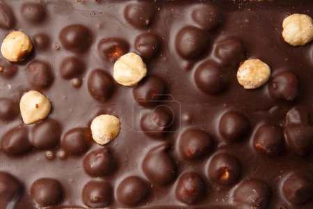 Téléchargez les photos : Background of dark chocolate and hazelnuts. Black handmade chocolate with nuts top view macro shot. - en image libre de droit