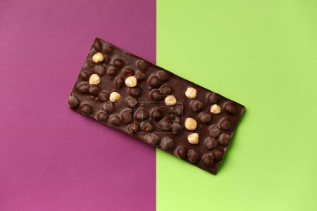 Photo for Handmade black chocolate with whole hazelnuts on a bright green and lilac background top view with space for text. - Royalty Free Image