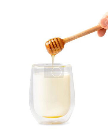 Foto de La miel fluye de una olla de madera en un vaso de leche sobre un fondo blanco. Gotas de miel que fluyen de una cuchara de miel a la leche. Foto conceptual de la leche y la miel sobre el aislamiento. - Imagen libre de derechos