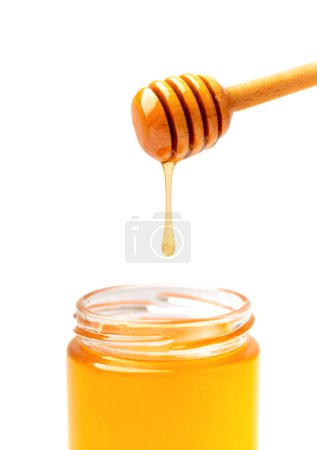 Foto de La miel orgánica se vierte de un cazo en un frasco transparente de vidrio de cerca sobre un fondo blanco. La miel fluye del palo de miel en el frasco. El vertido de la miel de la cacerola al aislamiento. - Imagen libre de derechos