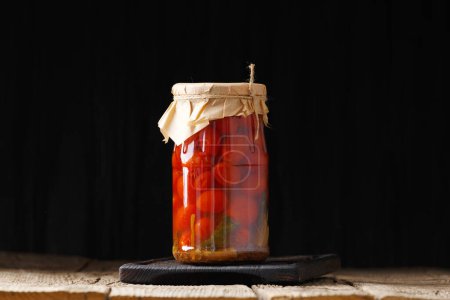 Téléchargez les photos : Tomates cerises marinées dans des bocaux en verre avec couvercles artisanaux avec poivre, aneth, basilic, ail sur un fond en bois close-up. Composition des tomates en conserve maison - en image libre de droit