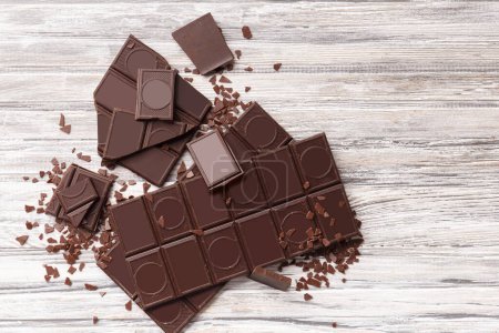 Photo for A whole bar of dark chocolate, broken pieces and chocolate chips on a gray wooden background top view with space for text, chocolate background. - Royalty Free Image
