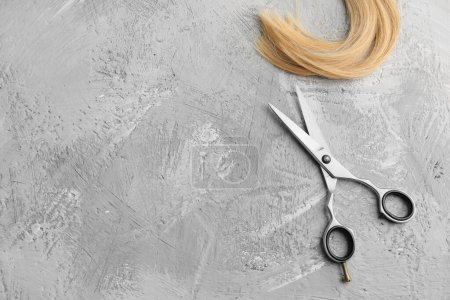 Foto de Scissors and piece of blond hair. Professional barber hair cutting shears on background. Hairdresser salon equipment concept, premium hairdressing set. Accessories for haircut with copy space - Imagen libre de derechos