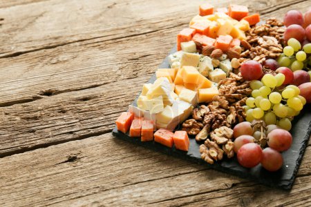 Photo for Different types of delicious cheese, nuts, grapes on a wooden background. Cheese platter: brie, camembert, blue cheese, emmental, parmesan, goat cheese, honey, grapes, walnuts, almonds. Healthy food. Fresh appetizing snack. - Royalty Free Image