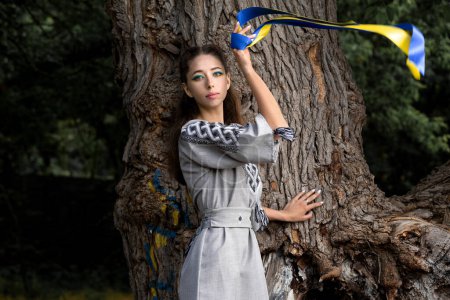 Téléchargez les photos : Une jeune fille en vêtements ukrainiens nationaux avec un ruban bleu et jaune. Le symbole de l'Ukraine. Guerre en Ukraine. La douleur de l'Ukraine. - en image libre de droit