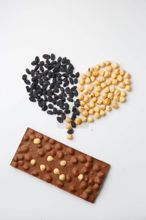 Foto de Black chocolate with nuts isolated. Dark chocolate on a white background. Conceptual chocolate, raisins and nuts in the shape of a heart. - Imagen libre de derechos