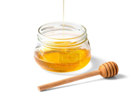 Photo for Honey is poured into an empty glass transparent jar and a wooden dipper on a white background close-up. Organic honey flows into a bowl on isolation. Pouring honey macro photography - Royalty Free Image