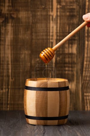 Foto de La miel se vierte de un cazo en un barril de madera sobre un fondo de madera. El concepto de productos orgánicos y naturales. - Imagen libre de derechos