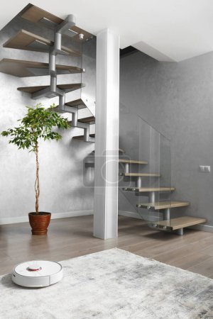 Téléchargez les photos : Un escalier avec marches en bois et une balustrade en verre, une colonne, une fleur intérieure, un robot aspirateur dans un intérieur moderne d'un appartement, une maison. Conception d'escaliers pour les locaux résidentiels. - en image libre de droit