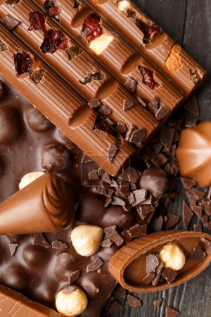 Photo for Dark chocolate with hazelnuts, milk chocolate with raisins and nuts, candies, chocolate chips on a dark wooden background close-up top view. The concept of varieties of chocolate. - Royalty Free Image