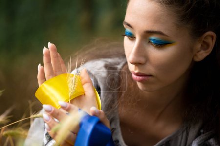 Téléchargez les photos : Une jeune fille avec un ruban bleu et jaune garde une oreille de blé. L'Ukraine nourrit le monde de céréales. Guerre en Ukraine. La douleur de l'Ukraine. Symbole du peuple ukrainien. - en image libre de droit