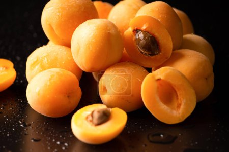 Téléchargez les photos : A handful of ripe apricots on a dark background. Useful fruit. Pineapple apricots on black background - en image libre de droit