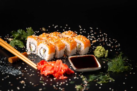 Téléchargez les photos : Set of salmon rolls on a dark background with chopsticks, sauce and red ginger. Red sushi with sesame on black background - en image libre de droit