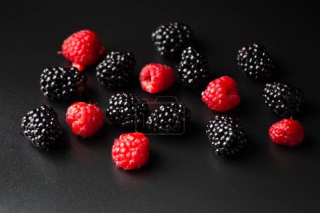 Téléchargez les photos : A handful of raspberries and blackberries on a black background close-up. Healthy fruits on a dark background with water drops - en image libre de droit