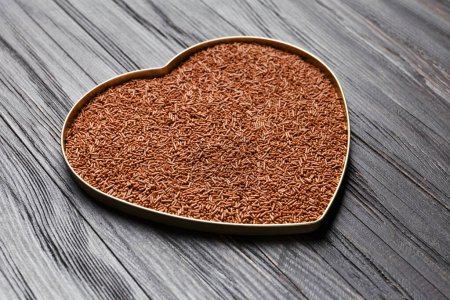 Photo for Chocolate chips in a heart-shaped box on a dark wooden background. - Royalty Free Image