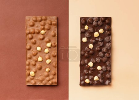 Foto de Chocolate negro y leche hecho a mano con avellanas en una vista superior de fondo marrón y beige. Fondo de chocolate. - Imagen libre de derechos