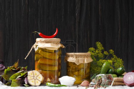 Photo for Pickled cucumbers in a jar, fresh gherkins, red and green chili, dill, basil, garlicn on a dark wooden background. Peppers, onions and fresh gherkins for preservation. Cucumber salad. - Royalty Free Image