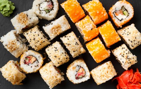 Foto de Set de rollos de salmón sobre fondo oscuro con salsa y jengibre rojo. Sushi rojo con sésamo sobre fondo negro - Imagen libre de derechos