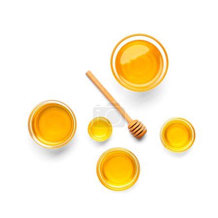 Foto de Composición creativa de miel en cuencos de vidrio de diferentes tamaños y una cacerola de madera en una vista superior de fondo blanco. Miel orgánica y cuchara de miel en aislamiento. - Imagen libre de derechos
