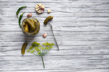 Photo for Pickled cucumbers in an open jar, gherkin on a fork and garlic on a light wooden background, top view, copy space. Homemade canned cucumbers. - Royalty Free Image