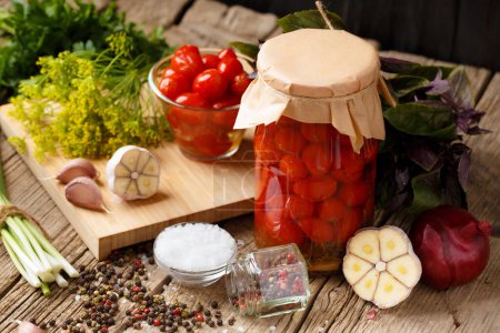 Téléchargez les photos : Marinated cherry tomatoes with garlic, dill and spices. Homemade canned tomatoes in closed jars with craft lids, fresh hot peppers and tomatoes on a wooden background. Pickled vegetables. - en image libre de droit