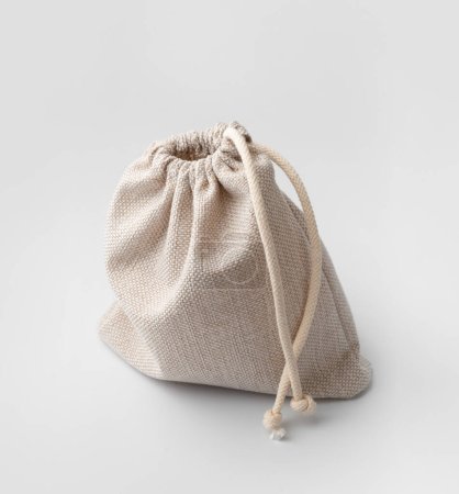 Téléchargez les photos : Un sac en tissu naturel léger avec un cordon isolé sur un fond blanc. Pochette en tissu grossier avec cordon. Pochette en tissu fermée. - en image libre de droit