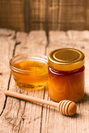 Photo for Creative composition of honey in a glass jar and a bowl, a wooden dipper on an aged wooden background. The concept of organic bee products. - Royalty Free Image