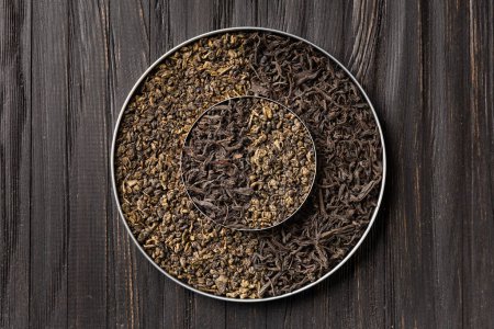 Photo for Conceptual composition of dry leaves of black and green tea in a round bowl on a wooden background top view with space for text. Green and black tea on a dark background. - Royalty Free Image