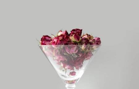 Téléchargez les photos : Buds of pink roses in a martini glass isolated. Buds of dried flowers in a glass goblet on a white background. Dried flower tea. Valentine's Day. - en image libre de droit