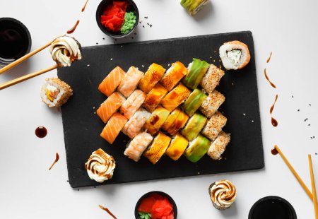 Téléchargez les photos : Ensemble rouleau avec saumon, avocat et anguille sur une planche de pierre avec wasabi et sauce soja sur un fond gris vue de dessus - en image libre de droit