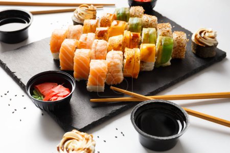 Téléchargez les photos : Rouler avec du saumon, de l'avocat, des crevettes et de l'anguille sur une planche de pierre avec du wasabi et de la sauce soja sur un fond gris - en image libre de droit