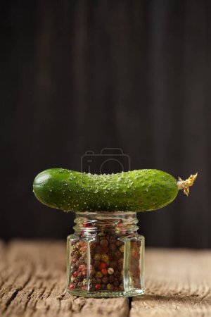 Photo for Hot pepper and fresh cucumber on a wooden background. A fresh cucumber lies on a jar of pepper close-up. - Royalty Free Image