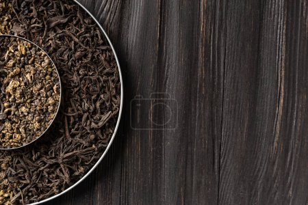 Photo for Conceptual composition of dry leaves of black and green tea in a round bowl on a wooden background top view with space for text. Green and black tea on a dark background. - Royalty Free Image