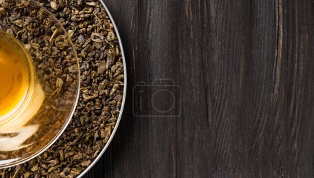 Photo for Composition of dry green tea leaves, roasted coffee beans in a round box and tea in a cup on a dark wooden background top view close-up with space for text. - Royalty Free Image