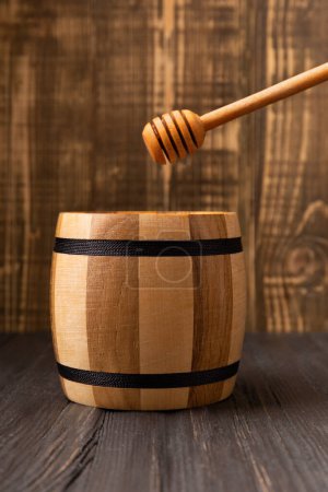Photo for Wooden barrel for honey and dipper on a dark wooden background. Utensils for honey from natural materials. - Royalty Free Image