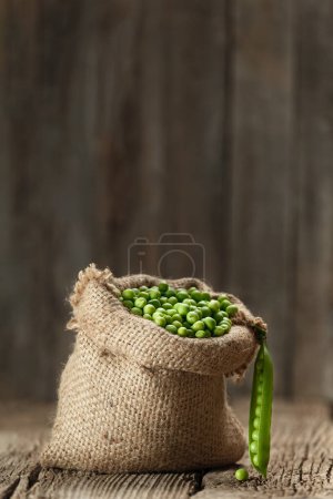 Photo for Fresh organic peeled green peas in a burlap bag, open green pea pods on an aged wooden background, copy space. Vegetable protein, healthy products. - Royalty Free Image