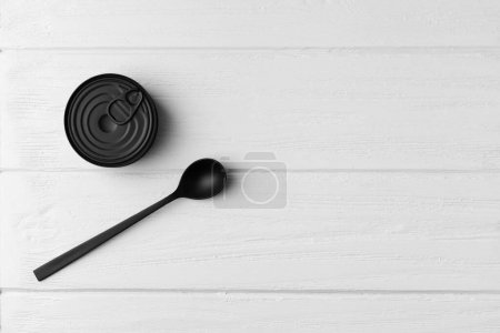 Foto de Lata cerrada redonda mate negra y cuchara negra sobre fondo de madera gris vista superior con espacio para texto, conservas, conservas. - Imagen libre de derechos