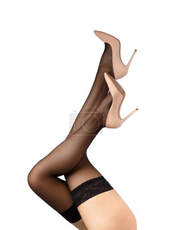 Schlanke Frauenbeine in schwarzen Strümpfen mit schönem durchbrochenen Gummizug und eleganten beigen High Heels auf weißem Hintergrund, isoliert. Nahaufnahme der anmutigen Beine eines Mädchens in Strümpfen